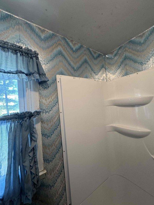 Completed installation of walk-in shower unit in RV bathroom, featuring white molded fiberglass construction with integrated shelving recesses. Mounted chrome shower head assembly on curved arm extension and installed decorative chevron-patterned tile work on upper walls in blue, teal, and beige tones to complement existing bathroom design.