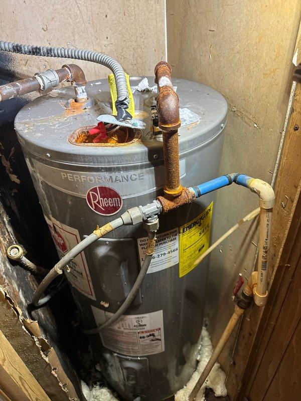 Responded to service call for water leak affecting the water heater and under-sink plumbing. Upon inspection, identified active leaking from corroded copper piping at the top of the Rheem Performance water heater, with additional leak present at the under-sink connection. The copper pipes exhibited significant oxidation, rust-colored patina, and corrosion throughout the vertical sections and connection points, indicating advanced deterioration of the plumbing system. Documented existing conditions with photographs showing the extent of corrosion on all copper connections, the water heater installation, and surrounding plumbing infrastructure. Provided assessment of the compromised piping and recommended necessary repairs to address the active leaks and prevent further water damage to the water heater and surrounding area.