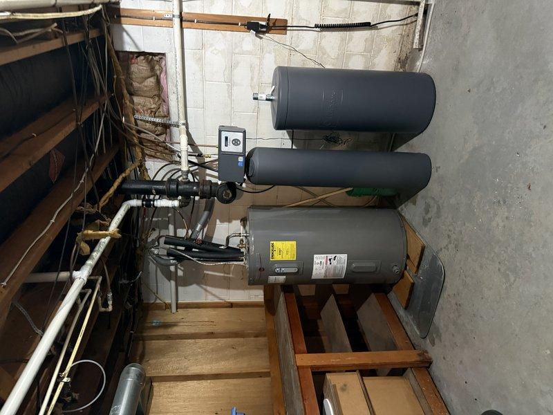 Responded to water leak reported on line coming from water heater in basement mechanical room. Upon arrival, inspected water heater and associated plumbing connections, including copper piping, brass valves, and supply lines. Identified leak source at corroded section of copper pipe near shutoff valve assembly below water heater. Assessed condition of existing plumbing infrastructure, noting age-related deterioration on copper piping and fittings. Documented equipment configuration including horizontally-mounted pressure tanks, water heater unit on wooden platform, and interconnected piping systems. Leak was isolated and repairs completed to restore proper water flow and eliminate active water discharge.