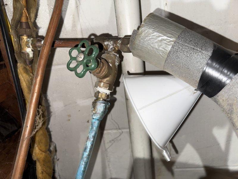 Responded to water leak reported on line coming from water heater in basement mechanical room. Upon arrival, inspected water heater and associated plumbing connections, including copper piping, brass valves, and supply lines. Identified leak source at corroded section of copper pipe near shutoff valve assembly below water heater. Assessed condition of existing plumbing infrastructure, noting age-related deterioration on copper piping and fittings. Documented equipment configuration including horizontally-mounted pressure tanks, water heater unit on wooden platform, and interconnected piping systems. Leak was isolated and repairs completed to restore proper water flow and eliminate active water discharge.