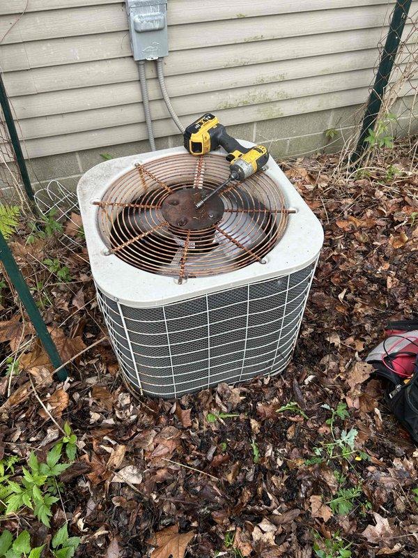 Serviced outdoor air conditioning condenser unit with heavily corroded fan guard assembly. Replaced rusted fan guard and associated mounting hardware due to extensive rust and corrosion that compromised structural integrity and posed safety concerns. Cleared accumulated debris, leaves, and organic matter from around unit base to restore proper airflow and prevent future operational issues.