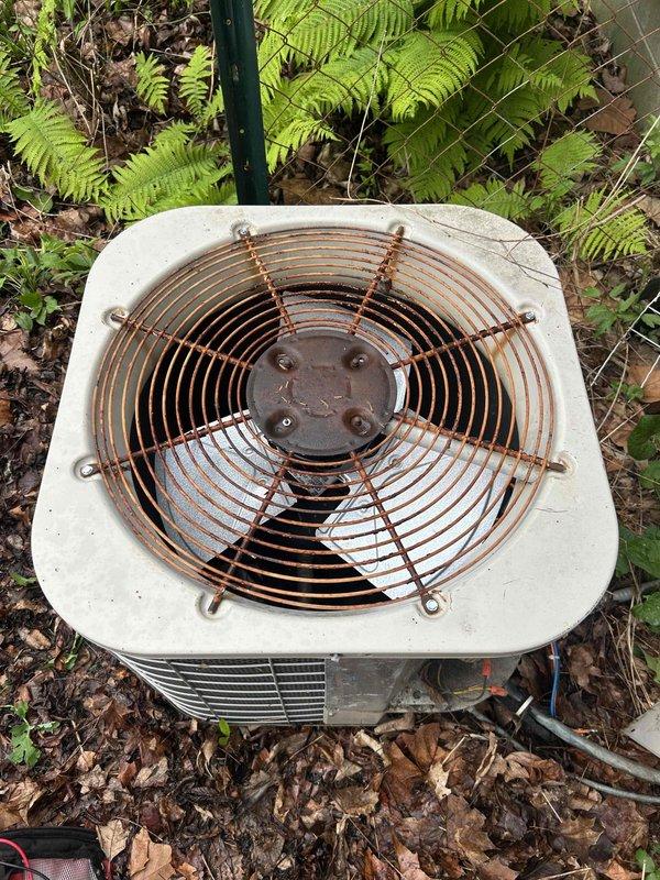 Serviced outdoor air conditioning condenser unit with heavily corroded fan guard assembly. Replaced rusted fan guard and associated mounting hardware due to extensive rust and corrosion that compromised structural integrity and posed safety concerns. Cleared accumulated debris, leaves, and organic matter from around unit base to restore proper airflow and prevent future operational issues.