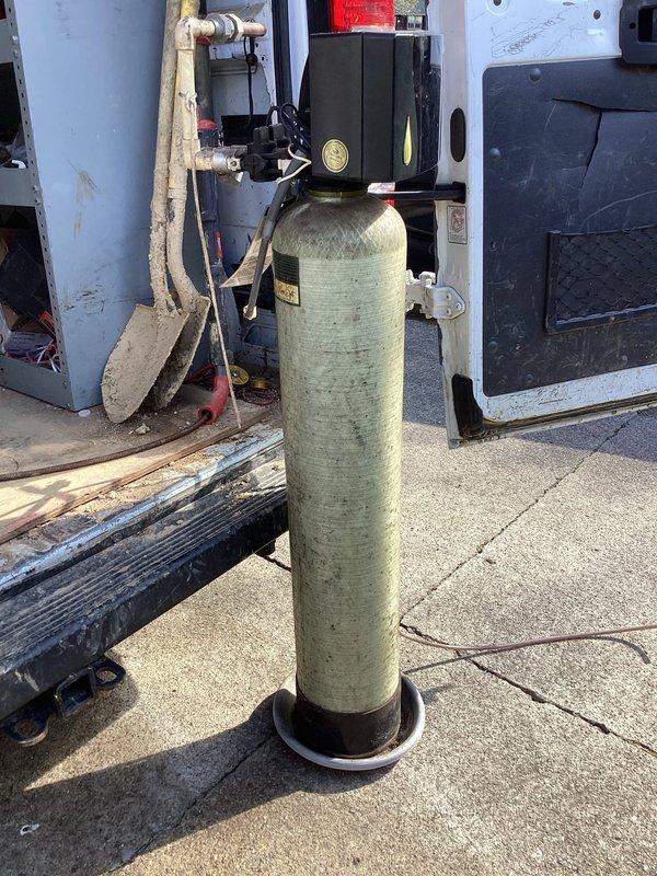 Completed installation of residential water softener system. Installed new water softener tank with control valve assembly and brine tank in exterior location. Connected unit to existing water supply line using PVC piping, brass compression fittings, and appropriate shut-off valves. Configured under-sink plumbing connections with T-junction distribution system to integrate softener bypass. Installed electrical components for automatic regeneration cycle control. Secured all connections with metal hose clamps and tested system for proper operation and leak-free performance. Unit is fully operational and programmed for optimal water conditioning.