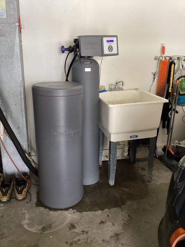 Completed monthly prepaid plumbing inspection of residential property. Identified and documented minor leaks at bathroom tub spout and water softener connections in basement utility area. Inspected bathroom fixtures including chrome shower control valve, tub spout, and drain assembly, noting proper operation of temperature control mechanism. Examined Culligan water softening system with dual tank configuration, checking control head unit functionality and connection integrity at inlet/outlet points with blue handle valve. Photographed areas of concern for maintenance records, including visible water staining on basement concrete floor near water treatment equipment. All fixtures and plumbing components documented for ongoing maintenance tracking.