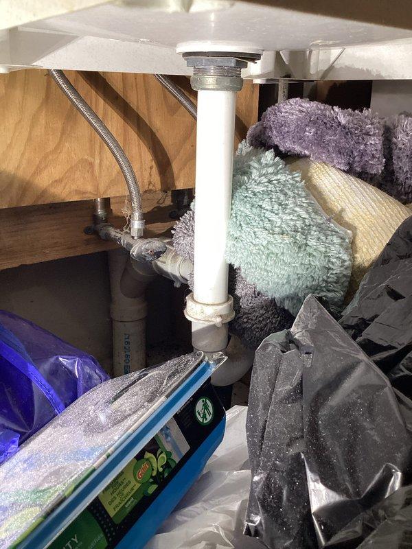 Completed monthly membership plumbing inspection of residential property. Inspected washing machine supply valves and connections, noting aged brass valves with blue handles, foam-insulated hot and cold supply lines, and corrugated flexible drain hose—all connections secure with no active leaks detected. Examined under-sink plumbing including PVC drain assembly and braided supply line with shutoff valve, confirming proper operation and drainage with no visible leaks or immediate concerns requiring attention.