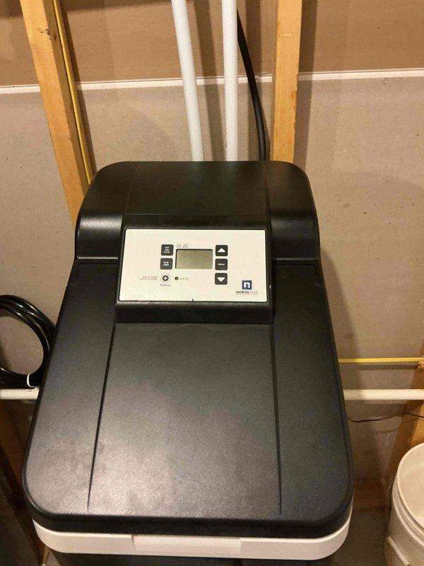 Responded to warranty call for water softener with salt bridging issue on unit installed less than one year prior. Inspected system and confirmed proper operation of replacement water softener unit. Control panel displaying normal parameters with digital display functioning correctly. Verified plumbing connections secure with no leaks present at inlet/outlet PVC piping. Unit positioned properly on base platform with adequate clearance for service access and maintenance.