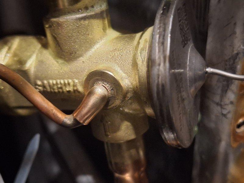 Returned to site to complete warranty repair by installing replacement thermostatic expansion valve (TXV) on the refrigeration system. Removed failed TXV assembly and brazed new valve into copper refrigerant lines, ensuring proper connection to the brass valve body and actuator assembly. Verified secure mounting and proper sensor bulb placement for accurate superheat control. System tested and operational upon completion.
