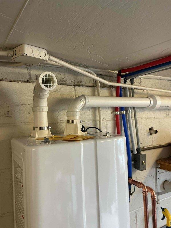 # Tankless Water Heater Installation

Successfully installed a new Energy Star certified tankless water heater unit in basement utility area. Mounted unit securely to concrete block wall and established all necessary water supply connections using copper piping for both hot and cold water lines. Installed isolation valves with color-coded handles (red for hot, blue for cold) at the unit connections to facilitate future maintenance and servicing. 

Configured PVC venting system with proper elbow joints and termination fittings to ensure safe exhaust of combustion gases. Routed vent piping along ceiling and wall with appropriate support brackets to meet manufacturer specifications and local code requirements. Integrated existing copper supply lines with new installation, securing all piping runs with mounting brackets for stability and professional appearance.

Programmed digital control panel and verified proper operation of the unit. Confirmed all connections are leak-free and system i