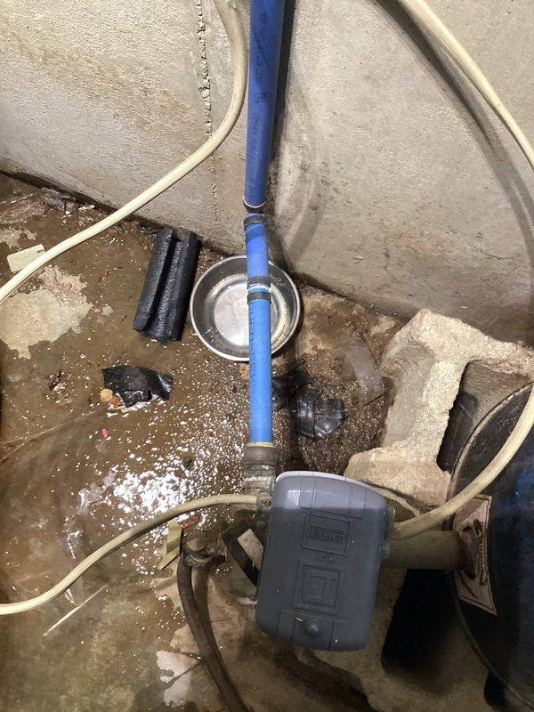 Responded to service call for slow water leaks in residential plumbing system. Upon arrival, conducted thorough inspection of basement utility area and identified active leakage in main water supply lines. Inspected blue PVC vertical drain line with metal mounting bracket and gray pump control junction box, noting moisture accumulation and mineral deposits on concrete floor indicating chronic seepage. Examined flexible supply tubes and connections for signs of deterioration or loose fittings. Assessed black filter component and associated plumbing fixtures for proper operation and seal integrity. Documented existing conditions with photographic evidence showing efflorescence patterns on concrete surface and debris accumulation consistent with ongoing moisture infiltration. Provided diagnosis of leak sources and recommended corrective actions to address water intrusion issues and prevent further damage to basement area.