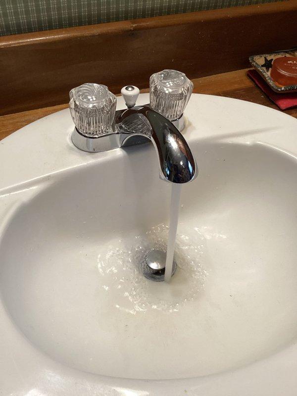 Replaced bathroom faucet assembly including chrome spout, dual acrylic knob handles with mounting plate, and aerator. Connected new flexible braided stainless steel supply lines to shutoff valves and verified proper water flow and drainage through existing P-trap assembly with no leaks detected.