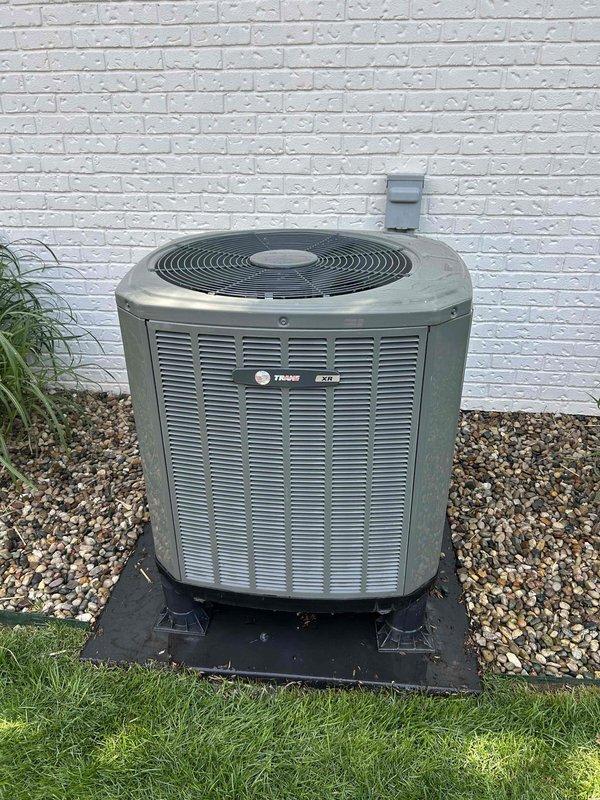 Responded to no heat/no cool complaint on residential HVAC system. Upon arrival, performed diagnostic evaluation of Trane air conditioning condenser unit and associated heating system. Inspected outdoor condensing unit, which showed signs of weathering and age but appeared structurally intact with proper mounting on equipment pad. Verified unit placement, clearances, and electrical disconnect box installation. Documented system condition through photographic records showing equipment positioning against structure, gravel base installation, and overall unit appearance. System requires further troubleshooting to identify root cause of complete heating and cooling failure, as initial visual inspection of outdoor components did not reveal obvious mechanical damage or obstruction to airflow through louvered panels and fan grille.