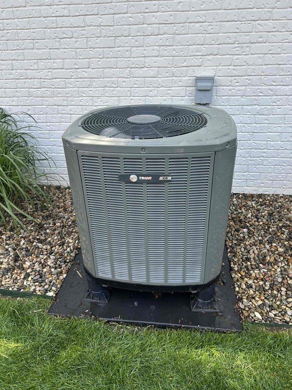 Responded to no heat/no cool complaint on residential HVAC system. Upon arrival, performed diagnostic evaluation of Trane air conditioning condenser unit and associated heating system. Inspected outdoor condensing unit, which showed signs of weathering and age but appeared structurally intact with proper mounting on equipment pad. Verified unit placement, clearances, and electrical disconnect box installation. Documented system condition through photographic records showing equipment positioning against structure, gravel base installation, and overall unit appearance. System requires further troubleshooting to identify root cause of complete heating and cooling failure, as initial visual inspection of outdoor components did not reveal obvious mechanical damage or obstruction to airflow through louvered panels and fan grille.