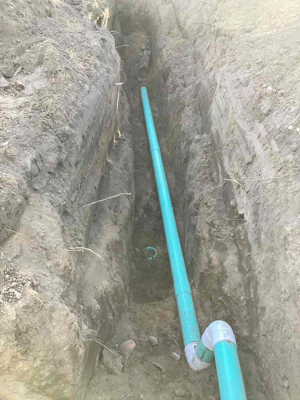 Excavated trench from foundation to road and installed new turquoise PVC sewer line with proper fittings and Y-junction connections. Replaced deteriorated sewer line section, connected to existing vertical drain pipes at foundation wall, backfilled trench, and ensured proper drainage slope throughout the installation.