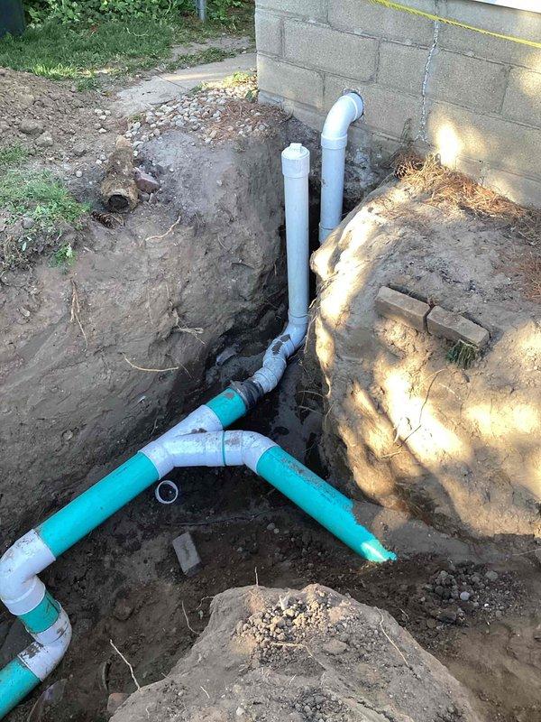 Excavated trench from foundation to road and installed new turquoise PVC sewer line with proper fittings and Y-junction connections. Replaced deteriorated sewer line section, connected to existing vertical drain pipes at foundation wall, backfilled trench, and ensured proper drainage slope throughout the installation.