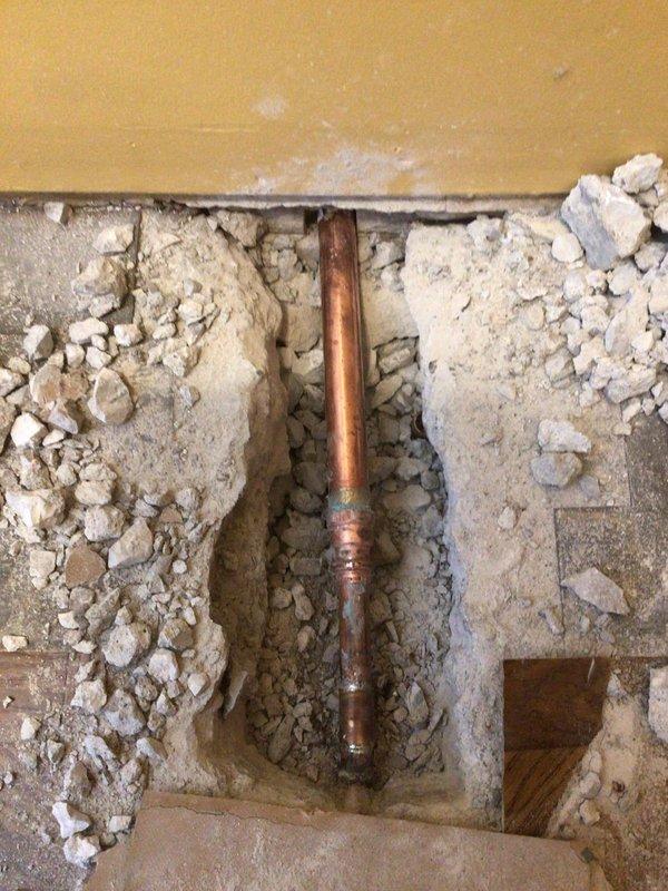Responded to water leak at main plumbing entry point beneath concrete foundation. Performed demolition work to expose copper supply line running vertically through concrete substrate, revealing leak at underground connection point. Removed concrete flooring and wall material to access compromised piping with threaded fittings. Assessed two exterior hose bibs mounted in concrete foundation showing signs of deterioration, water staining, and potential failure requiring replacement to prevent continued water intrusion and foundation damage.