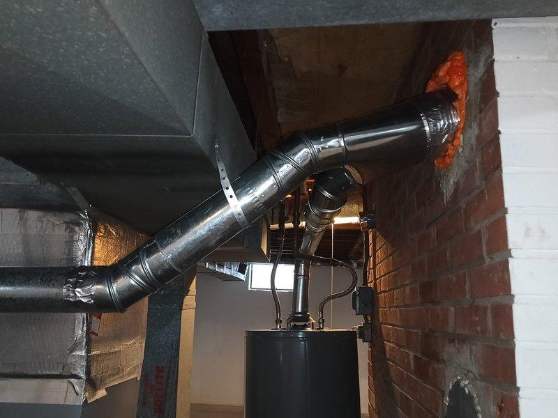 Completed 6-inch flue liner replacement for existing HVAC system. Removed old deteriorated liner and installed new metallic flue pipe through existing brick chimney penetration. Secured new ductwork to furnace unit with proper metal straps and fasteners, ensuring all seams and joints were sealed with aluminum tape for airtight connections. Applied expanding foam insulation around the chimney penetration point to seal gaps and prevent air infiltration. Installed reflective metallic barrier within the circular opening to protect against heat transfer and maintain proper clearances per manufacturer specifications and code requirements.