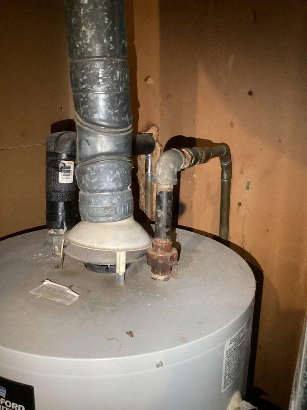 Conducted on-site assessment of existing residential water heater installation in utility area. Documented current condition of unit including top-mounted components, pressure relief system, venting configuration, and supply line connections. Evaluated galvanized vent pipe showing age-related deterioration and water staining, copper supply lines with visible oxidation and corrosion, and insulated water lines. Inspected shutoff valves, temperature/pressure relief valve assembly, and all pipe fittings for proper configuration. Photographed complete installation to provide comprehensive documentation for water heater replacement estimate including clearances, existing plumbing connections, venting pathway, and utility room conditions.