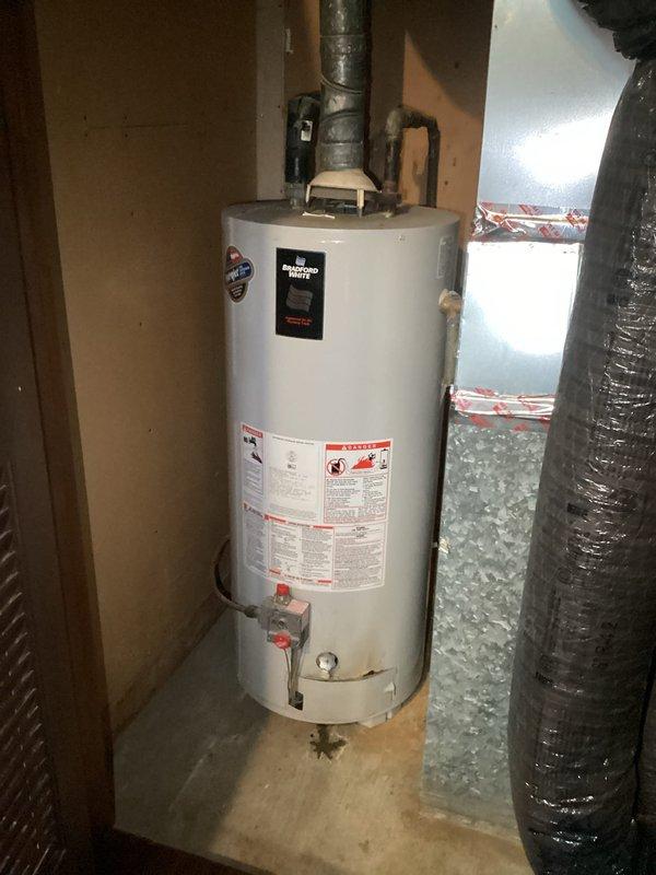 Conducted on-site assessment of existing residential water heater installation in utility area. Documented current condition of unit including top-mounted components, pressure relief system, venting configuration, and supply line connections. Evaluated galvanized vent pipe showing age-related deterioration and water staining, copper supply lines with visible oxidation and corrosion, and insulated water lines. Inspected shutoff valves, temperature/pressure relief valve assembly, and all pipe fittings for proper configuration. Photographed complete installation to provide comprehensive documentation for water heater replacement estimate including clearances, existing plumbing connections, venting pathway, and utility room conditions.