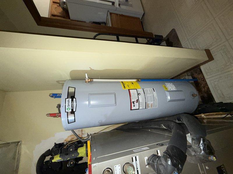 Completed warranty water heater installation in residential utility room. Removed existing unit and installed new light blue cylindrical water heater with proper plumbing connections, including hot and cold supply lines with shutoff valves. Unit positioned vertically adjacent to existing HVAC equipment in mechanical room with adequate clearance for service access and code compliance.