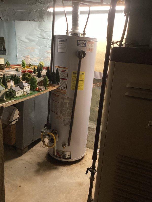 Responded to no hot water call for Kenmore water heater that experienced pilot light failure following recent basement flooding. Unit had previously recovered from a flood event four to five months prior but failed to relight after second flooding incident. Customer reported intermittent ignition attempts with brief flame and whooshing sound, followed by automatic shutdown after approximately 30 seconds, indicating likely thermocouple or gas valve safety lockout. Performed visual inspection of water heater and surrounding utility area, documented moisture exposure to unit and ductwork system. Photographed equipment condition showing water heater installation with connecting piping, flexible gas connectors, and evidence of water damage to basement mechanical space including condensation on metal ductwork.