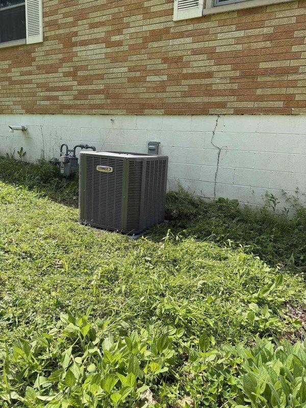 Completed installation of Lennox air conditioning system with matching evaporator coil at residential property. Unit was properly positioned on concrete pad against exterior wall, with refrigerant lines professionally routed through wall penetration and secured to building exterior. System was charged, tested, and verified operational with temperature measurements confirming proper performance at 25.9°F differential.