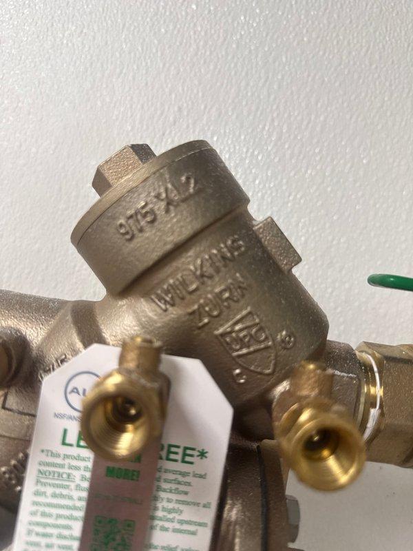 Inspected and serviced commercial backflow preventer assembly and associated isolation valves. The Watts brand backflow prevention device with test ports was examined for proper operation and compliance. Verified ball valve functionality with green handle actuator and confirmed all brass fittings and connections were secure. Documented equipment identification numbers and current system configuration for maintenance records.