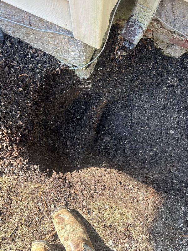 Installed exterior cleanout access point at building foundation to address drainage issue. Secured copper drain line with metal hose clamp and flexible conduit connection at ground level. Successfully cleared blockage and restored proper drainage flow through newly installed cleanout assembly.