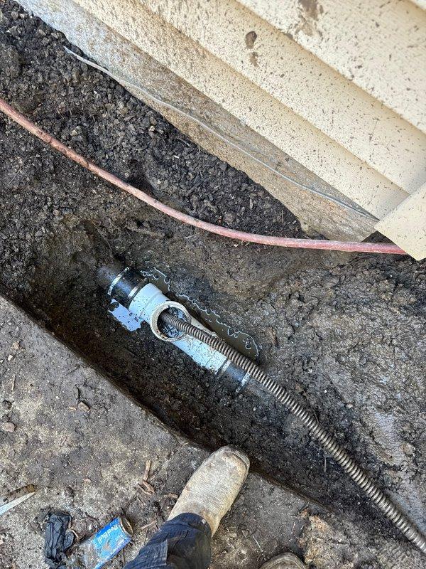 Installed exterior cleanout access point at building foundation to address drainage issue. Secured copper drain line with metal hose clamp and flexible conduit connection at ground level. Successfully cleared blockage and restored proper drainage flow through newly installed cleanout assembly.