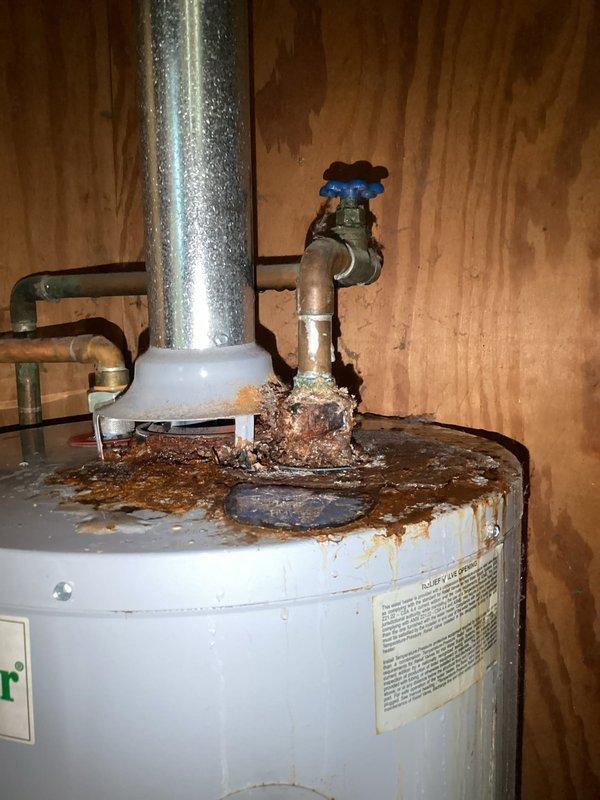 Responded to active water heater leak at residential property. Upon inspection, discovered a 2015 natural gas automatic storage water heater with severe corrosion and rust buildup at the top connections, particularly around the shutoff valve and copper pipe joints. The corrosion had compromised the integrity of the connections, resulting in active water leakage. Evidence of moisture damage was visible on surrounding wooden surfaces and extensive water staining on the wall, indicating prolonged exposure to leaking water. The metallic piping showed heavy condensation and deterioration. Documented the condition of the unit, including manufacturer specifications and serial number, along with the extent of corrosion damage for replacement recommendations.