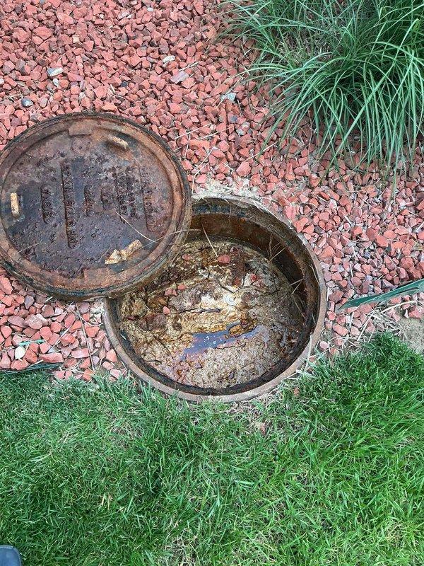 Responded to service call for multiple drains backing up into kitchen. Upon arrival, located and accessed exterior sewer cleanout at ground level near landscaping border. Removed heavily rusted cast iron sewer access cover, revealing chamber with accumulated debris, sediment, and organic matter buildup. Inspected secondary PVC cleanout access point in landscaped area, noting sediment accumulation on interior pipe walls. Performed mainline sewer clearing to address blockage causing backup in multiple interior drains. Verified proper drainage flow restored to all affected fixtures. Replaced cleanout covers and left access points secure.