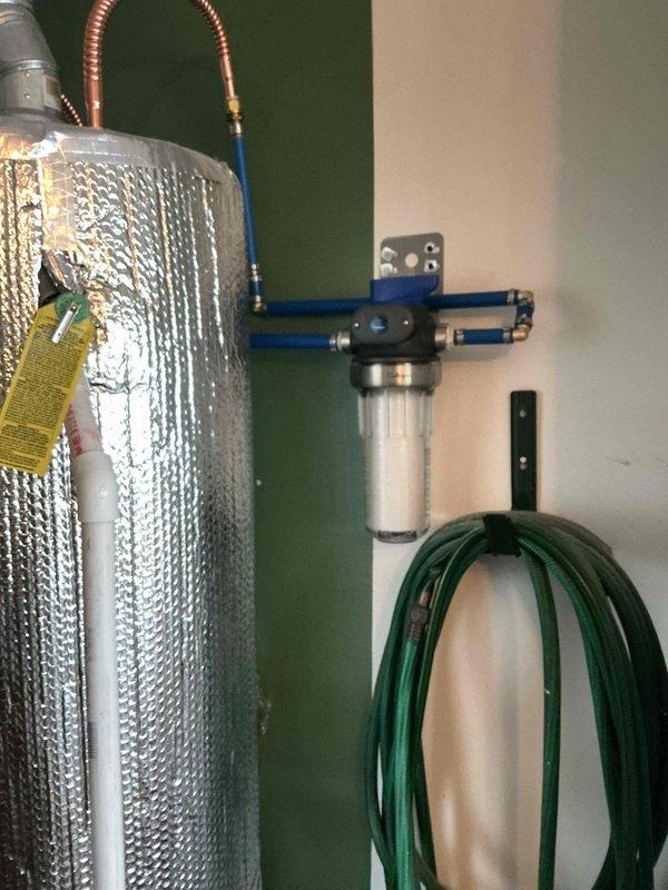 Installed a complete whole-house water filtration system on the main water supply line, including mounting the filter housing with clear cartridge chamber to the wall using secure brackets, connecting blue PVC supply piping, and integrating a brass shut-off valve with lever handle for system isolation and maintenance access. All connections were properly fitted and tested to ensure leak-free operation and optimal water flow throughout the residence.
