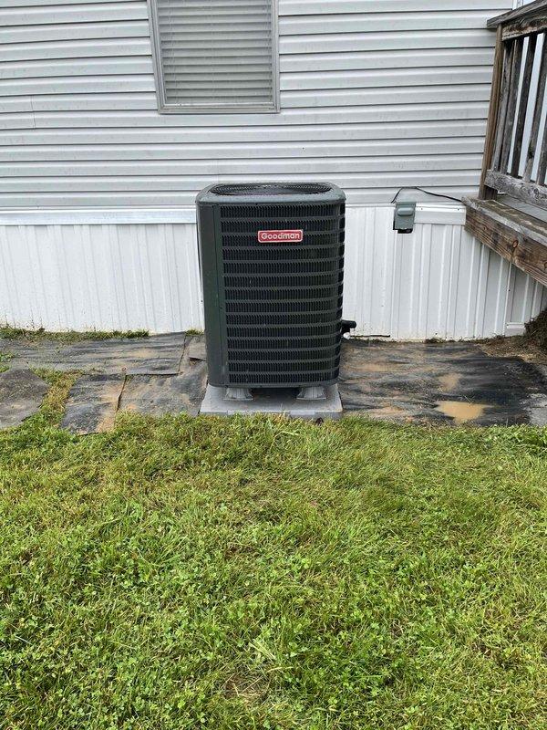 Completed full heat pump system installation at manufactured home, including outdoor Goodman condensing unit mounted on concrete pad with proper electrical conduit routing and indoor air handler with 18x20x1 filter specification. System installed per manufacturer specifications with all components operational and financing paperwork finalized.