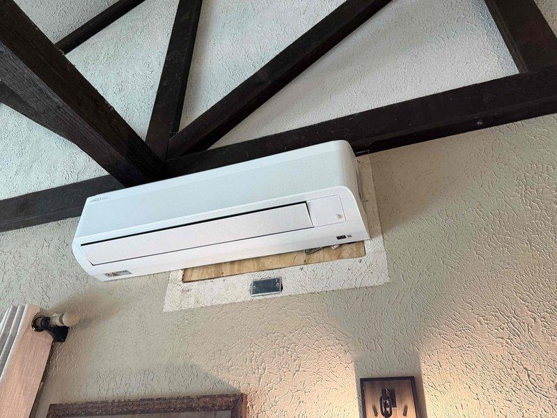 Completed installation of Lennox ductless mini-split system in residential property. Mounted indoor evaporator unit on interior wall beneath vaulted ceiling with exposed beam architecture, utilizing wooden backing board for secure attachment. Installed outdoor condenser unit on pad against exterior brick wall, established refrigerant line set and electrical connections via PVC conduit with proper mounting brackets, and verified system operation upon startup.