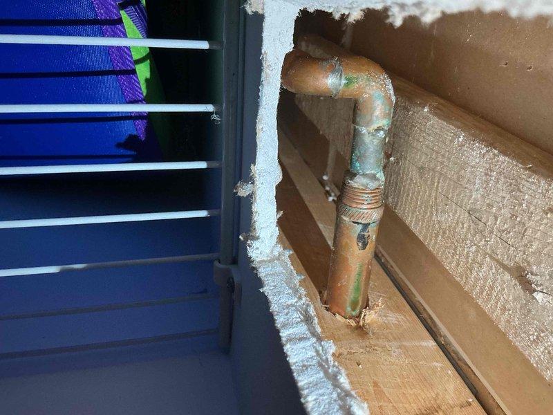 Responded to report of outdoor spigot leaking into basement. Upon inspection, located copper pipe penetration through exterior wall with significant deterioration of wall material and sealant around pipe entry point. Found evidence of water infiltration resulting in ice buildup on interior HVAC system components and surrounding surfaces, indicating active leak allowing moisture and cold air to enter conditioned space. Documented corroded copper piping with green patina, compromised wall penetration with exposed cardboard backing material, and frost accumulation on interior mechanical equipment. Identified need for pipe replacement, proper wall sealing, and restoration of weather barrier at penetration point to prevent further water damage and air infiltration.