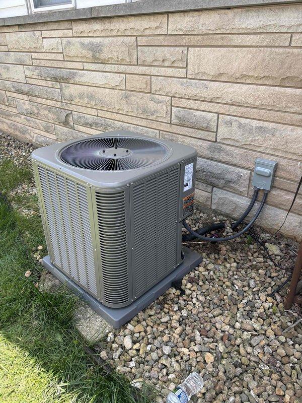 Completed installation of Lennox air conditioning system with matching evaporator coil. New outdoor condenser unit positioned on protective pad with gravel base, electrical disconnect box mounted to exterior wall with proper conduit routing and connections. System tested and verified operational with temperature readings confirming proper cooling performance.