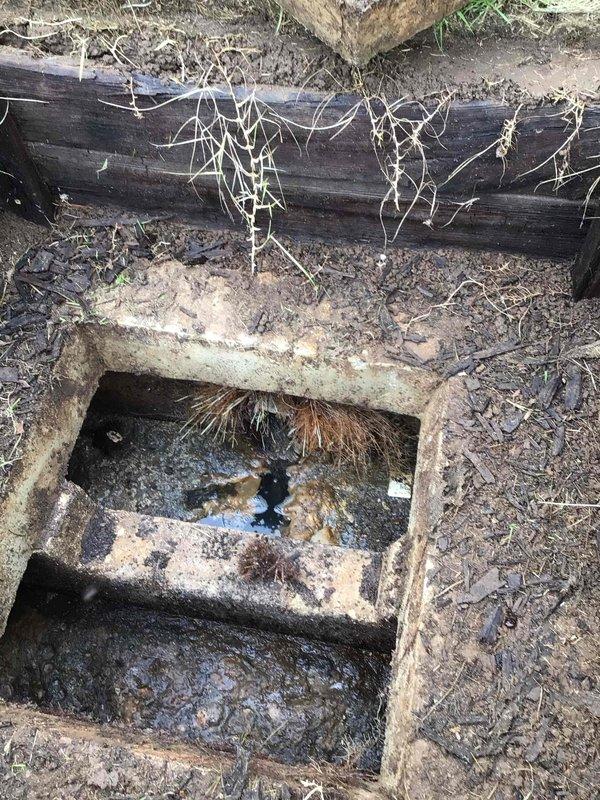 Responded to customer request for follow-up inspection of septic system access point after landscaping work involving bush removal. Upon arrival, conducted thorough visual assessment and photographic documentation of exposed septic tank lid and surrounding infrastructure. Inspection revealed deteriorated concrete septic tank access cover with significant weathering, surface erosion, and structural degradation from long-term environmental exposure. Documented condition of aging wooden railroad tie framing around access point, noting accumulated soil, organic debris, and root intrusion in immediate vicinity. Confirmed septic system access remains functional despite cosmetic deterioration, with no immediate signs of structural failure or compromised system integrity requiring emergency intervention.