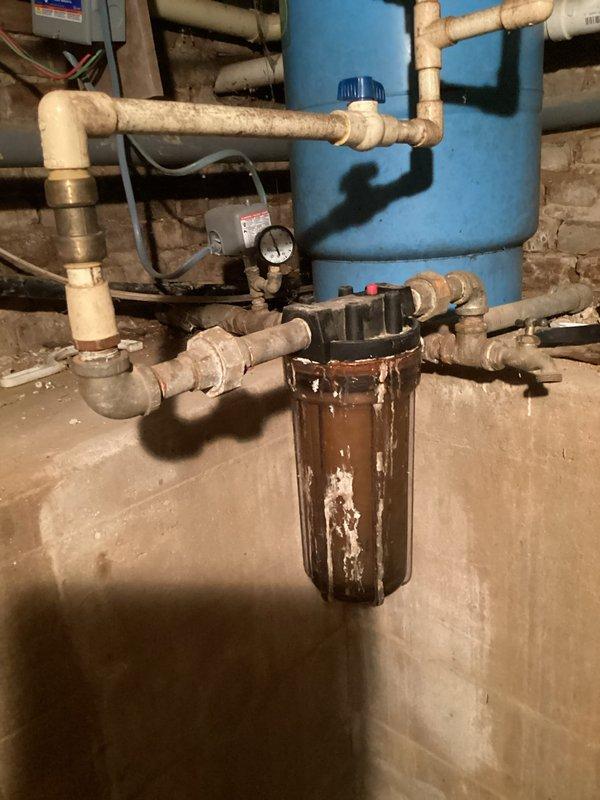 Responded to complaint of weak water pressure throughout home and trickling shower flow. Upon inspection, discovered severely corroded and deteriorated sediment filter housing in main water line system. The existing filter canister exhibited extensive rust buildup and scaling, causing significant flow restriction to entire plumbing system. Replaced failed filter housing and installed new American Plumber sediment filter cartridge. Verified proper connections to existing PVC piping network and water treatment system. Tested water pressure at multiple fixtures following replacement and confirmed restoration of adequate flow to shower and throughout residence.