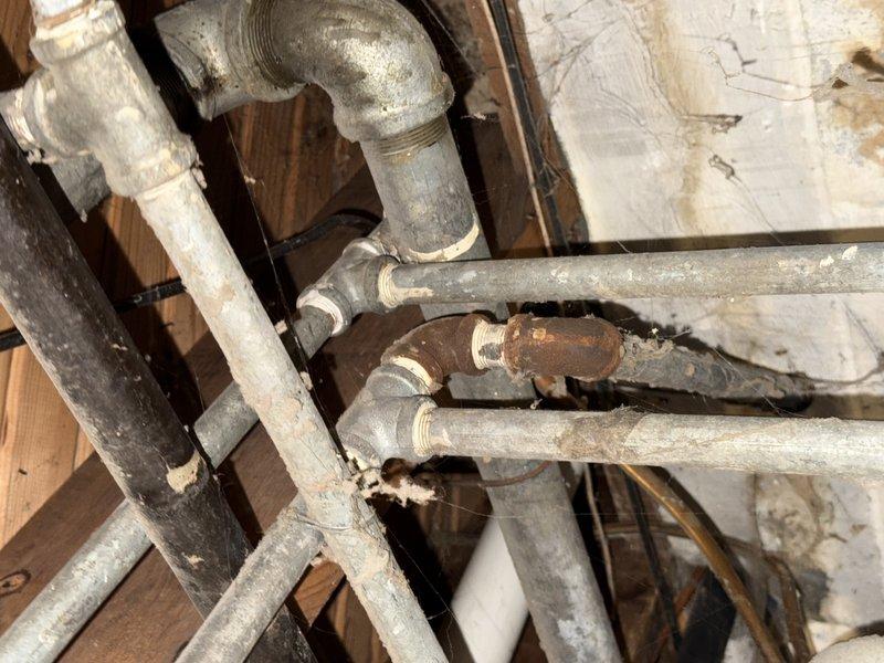 Responded to service call for reduced hot water flow while cold water pressure remained normal. Upon inspection of the crawl space plumbing system, identified corroded valve fitting on the hot water line as the source of the restriction. The galvanized piping showed significant age-related deterioration with visible rust accumulation on the affected valve component, which was impeding proper water flow. Documented the condition of the existing plumbing infrastructure, including the arrangement of supply lines, fittings, and structural mounting. Photographed the corroded valve assembly and surrounding pipe network for service records.