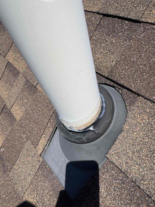 Inspected rooftop pipe penetration and documented deteriorated rubber boot flashing with visible tears, cracks, and split sections compromising weatherproof seal. Applied silicone flashing material to reinforce and seal damaged areas around PVC pipe penetration through asphalt shingle roof. Photographed existing conditions showing compromised flashing collar and completed repair work to prevent water infiltration at roof penetration point.