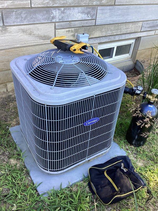 Responded to service call for Carrier air conditioning system with reported A-coil refrigerant leak, previously identified during last year's service when system was found low on refrigerant. Performed on-site inspection of outdoor condensing unit and documented equipment condition with photographs for service records.