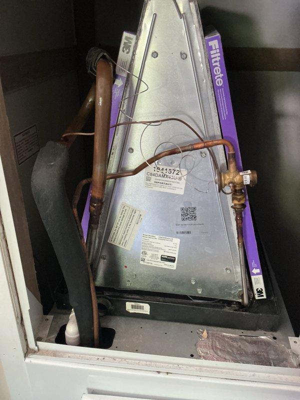 Completed rescheduled cooling system maintenance visit on attic-installed air handler unit with purple Filtrete washable filters in place. Performed basic monthly preventive maintenance inspection, verified refrigerant line connections and copper piping integrity showing normal age-related oxidation, confirmed proper drain pan positioning, and documented system operation with thermostat displaying 82°F at time of service.