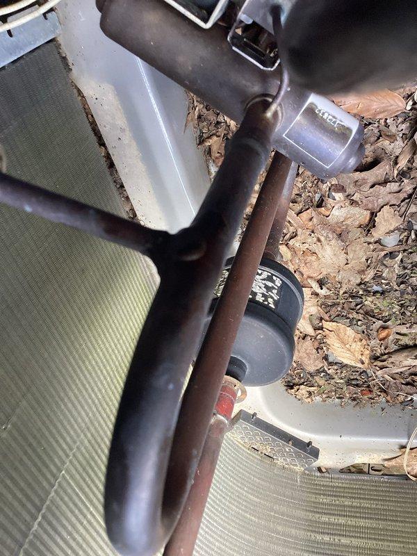 # HVAC Service Call - No Cooling Complaint

Responded to no cooling complaint on residential air conditioning system over 10 years old. Upon arrival, found outdoor condensing unit heavily obstructed by overgrown vegetation and debris accumulation in mulch bed surrounding equipment. Unit showed signs of age-related deterioration including oxidation on refrigerant lines and general weathering of components.

Cleared dense grass and weeds growing around condenser cabinet that were blocking airflow to unit and restricting proper ventilation through side panels. Removed leaves, organic debris, and accumulated material from around equipment base and refrigerant line penetrations. 

Inspected condenser coil fins which displayed discoloration and contamination buildup. Assessed refrigerant line insulation condition - noted degradation and exposure on suction line. Examined electrical disconnect and service panel mounted on exterior wall for proper operation.

Performed visual inspection of all