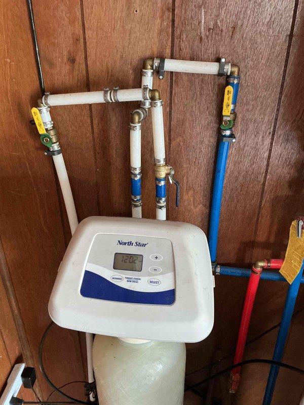 Completed re-installation of North Star water softener system in residential utility room. Properly configured all supply lines, drain connections, and brine system using color-coded PVC and copper piping with appropriate fittings and valves. Verified digital control head functionality displaying correct operational parameters, established proper electrical connection, and ensured integration with existing tankless water heater system. All plumbing connections tested and confirmed leak-free with system operational.