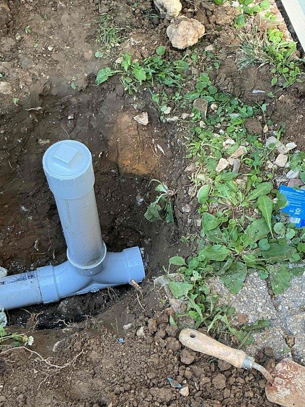 Performed camera inspection of exterior sewer cleanout located in yard area with overgrown vegetation. Excavated and accessed cleanout assembly, which consisted of a blue PVC T-fitting configuration with vertical access point and cap. Documented condition of cleanout system and surrounding area for maintenance records.