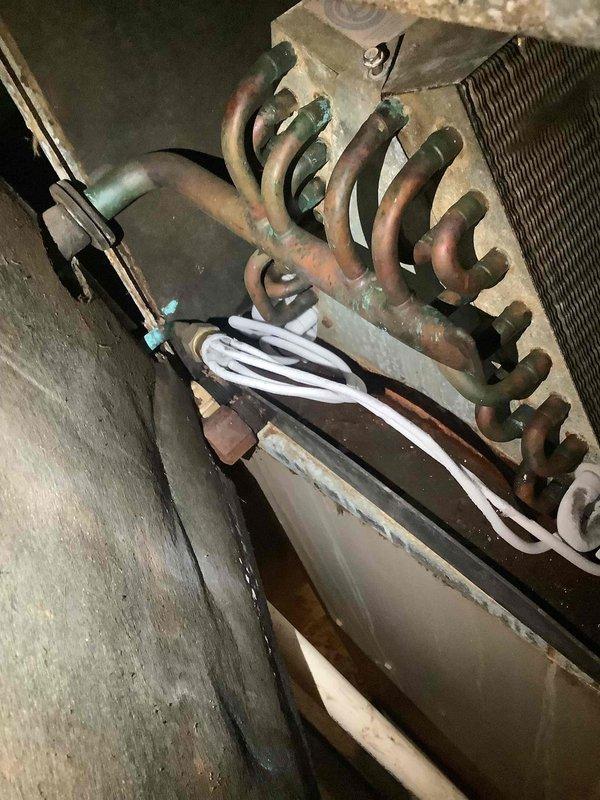 Responded to service call for air conditioning system not maintaining temperature at rental property. Upon inspection, discovered evaporator coil exhibiting severe corrosion with heavy oxidation throughout copper tubing, significantly reducing heat transfer efficiency and system cooling capacity. Thermostat reading 76°F indicated inadequate cooling performance. Documented condition of corroded coil assembly and discolored drain pan showing signs of age-related deterioration. Recommended evaporator coil replacement due to extent of corrosion compromising system operation.