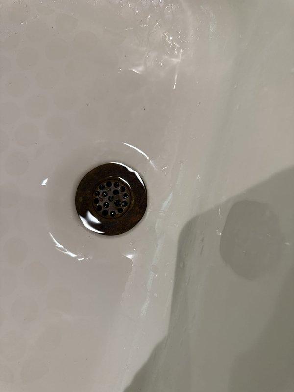 Responded to callback for tub drain that was not sealing properly. Upon arrival, inspected bathroom sink drain assembly and overflow components. Documented existing conditions showing moisture present in basin and decorative brass drain cover with perforations. Verified drain functionality and checked seal integrity on overflow drain cover visible in porcelain sink. Photographed faucet assembly, countertop area, and drain components for service records. Office waived trip fee for this return visit.