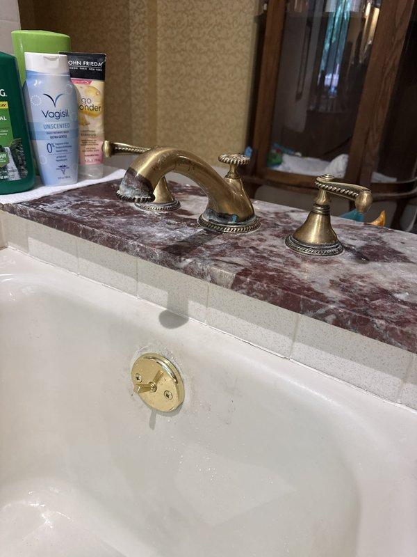 Responded to callback for tub drain that was not sealing properly. Upon arrival, inspected bathroom sink drain assembly and overflow components. Documented existing conditions showing moisture present in basin and decorative brass drain cover with perforations. Verified drain functionality and checked seal integrity on overflow drain cover visible in porcelain sink. Photographed faucet assembly, countertop area, and drain components for service records. Office waived trip fee for this return visit.