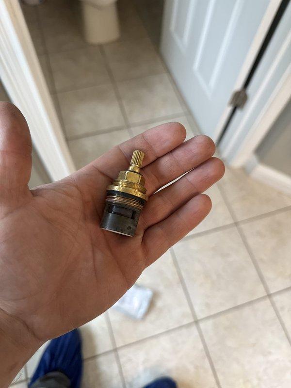 Responded to warranty service call for faucet cartridge replacement. Upon initial inspection, identified failed cartridge in wall-mounted fixture. Removed existing cartridge and verified specifications. Original part was unavailable on service vehicle. Photographed defective brass cartridge with knurled top, threaded stem, and rubber o-ring seals for reference. Return visit scheduled with correct replacement cartridge to complete installation and restore proper fixture operation.