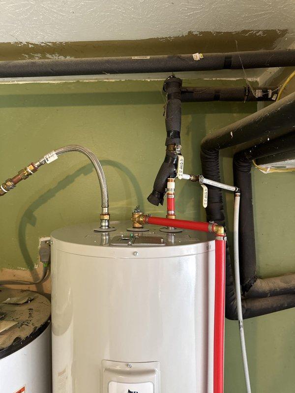 Responded to service call for reported water heater leak. Upon arrival, conducted thorough inspection of tanked water heater installation and surrounding plumbing connections. Examined all pipe fittings, valves, and connection points at the top of the unit, including the flexible metallic supply line, hot water outlet piping, and temperature and pressure relief valve discharge pipe. Inspected the tank exterior for signs of active leaking, corrosion, or moisture accumulation. Verified all brass fittings and copper connections were properly secured and showed no signs of seepage. Checked the condition of the water heater's base and surrounding floor area for water damage or pooling. All components appeared to be functioning within normal operating parameters at time of inspection, with no active leaks detected during the service visit.