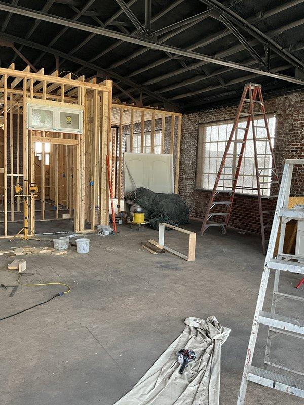 Conducted site assessment for complete HVAC system installation at commercial location undergoing full renovation with no existing equipment. Evaluated large open warehouse-style space with exposed ceiling joists, new interior wall framing, and concrete flooring to determine equipment sizing, placement, and ductwork routing requirements. Documented space layout including exposed brick walls, industrial windows, and ceiling structure to plan overhead venting installation through exposed beam system as requested.
